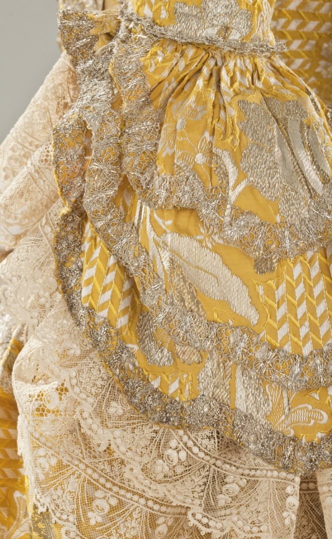 Detail sleeve, robe à la Francaise, England, c. 1760. Yellow silk plain weave with weft-float patterning and silk with metallic-thread supplementary-weft patterning, and metallic lace.